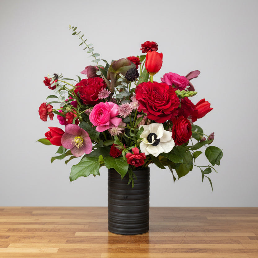 Bouquet of red, pink, and white Valentine's Day flowers in a black vase on a wooden table with a gray background